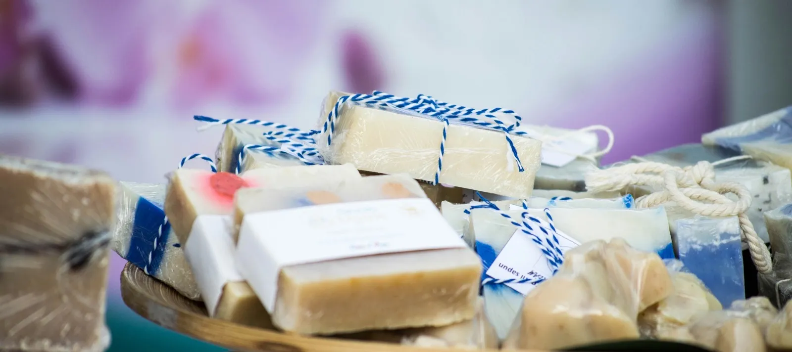 Sabonetes artesanais embalados em plástico com barbante azul e branco, um deles com rótulo de papel e etiqueta pendurada